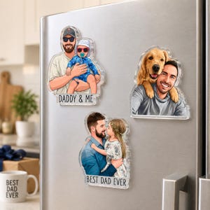 May include: Clear acrylic magnets with cartoon illustrations of a father with a baby, a dog, and a child. The magnets have the phrases "DADDY & ME" and "BEST DAD EVER" printed on them. The magnets are displayed on a silver refrigerator.