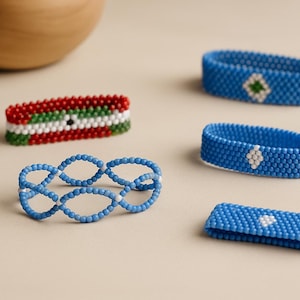 May include: A collection of beaded bracelets in different styles and colours. The bracelets are made with blue, red, white, and green beads. Some have geometric patterns, while others are a solid colour.