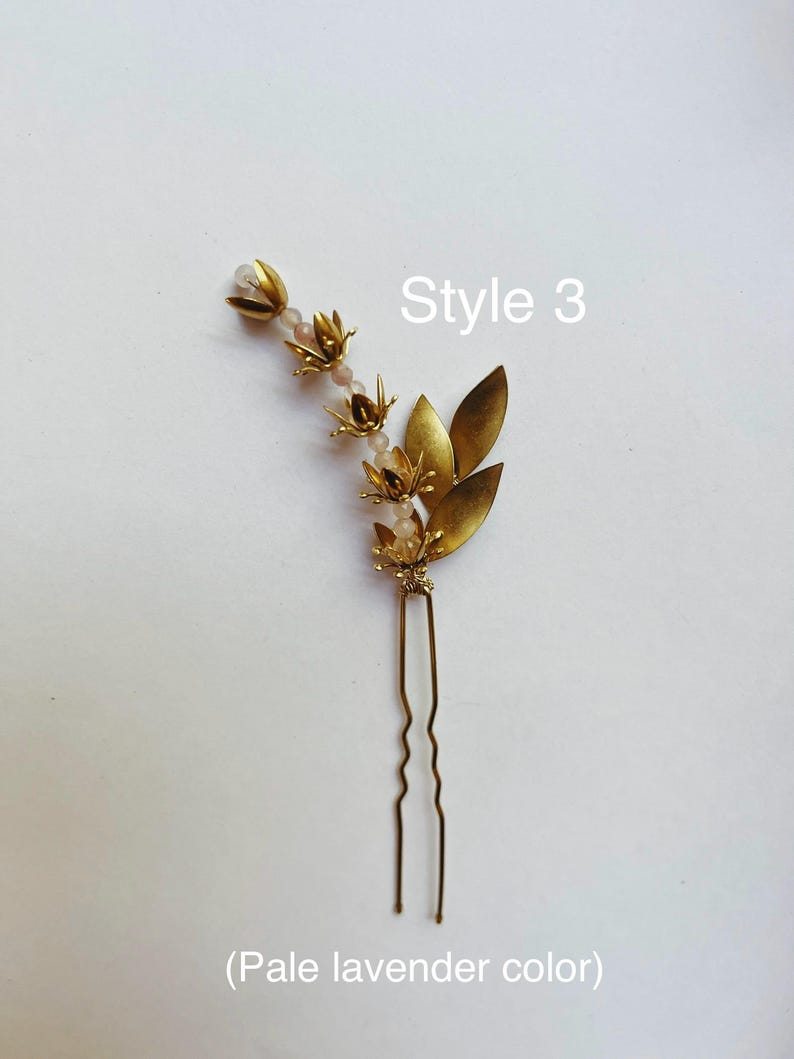 K&ouml;nnte beinhalten: Eine goldfarbene Haarnadel mit floralen und Blatt-Akzenten. Die Nadel hat kleine, detaillierte Bl&uuml;ten und Bl&auml;tter mit einer Ansammlung von helllavendelfarbenen Perlen. Der Text "Style 3" und "(Helllavendelfarben)" sind ebenfalls sichtbar.