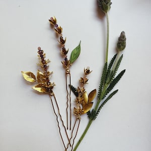 K&ouml;nnte beinhalten: Goldfarbene Haarnadeln mit Blumen- und Blattmotiven, verziert mit kleinen lila und rosa Perlen. Die Haarnadeln sind zusammen mit Lavendelzweigen angeordnet und zeigen ein nat&uuml;rliches, botanisches Thema. Ideal f&uuml;r Hochzeiten oder besondere Anl&auml;sse.