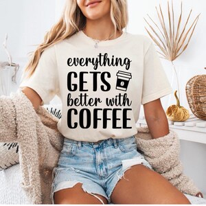 Könnte beinhalten: Cremefarbenes T-Shirt mit dem schwarzen Text "everything GETS better with COFFEE" und einer Kaffeetassen-Ikone. Das Shirt wird mit Jeansshorts kombiniert. Das Thema ist Kaffee und Freizeitkleidung.