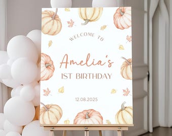 Può includere: Un cartello di benvenuto per un primo compleanno. Il cartello presenta zucche e foglie autunnali. Il testo recita "Benvenuti al 1° compleanno di Amelia" e la data 12.08.2025. Su un cavalletto.