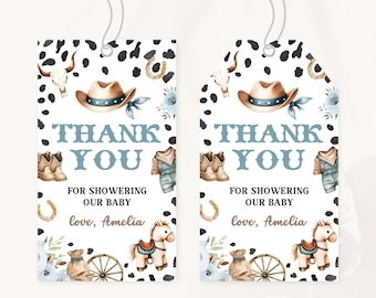 Könnte beinhalten: Zwei Geschenk-Anhänger im Cowboy-Thema mit einem schwarz-weißen Kuhfellmuster-Rand. Die Anhänger zeigen einen Cowboyhut, Stiefel und den Text "THANK YOU FOR SHOWERING OUR BABY". Die Anhänger sind mit floralen Akzenten und einem Spielzeugpferd verziert.