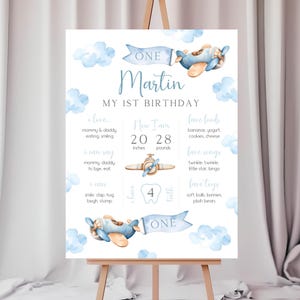 Puede incluir: Un cartel de hitos del primer cumplea&ntilde;os imprimible azul y blanco con un tema de avi&oacute;n de acuarela. El cartel presenta el nombre "Martin" y el texto "Mi primer cumplea&ntilde;os". Incluye detalles como la edad, la altura, el peso, los alimentos favoritos, las canciones y los juguetes del ni&ntilde;o.