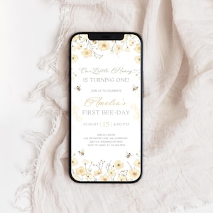 Peut inclure: Un smartphone affiche une invitation d'anniversaire sur le thème des abeilles. L'invitation présente des illustrations florales jaunes et blanches, avec le texte "Our Little Honey is Turning One!" et "Amelia's First Bee-Day."