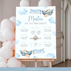 Puede incluir: Un cartel de hitos del primer cumplea&ntilde;os imprimible azul y blanco con un tema de avi&oacute;n de acuarela. El cartel presenta el nombre "Martin" y el texto "Mi primer cumplea&ntilde;os". Incluye detalles como la edad, la altura, el peso, los alimentos favoritos, las canciones y los juguetes.