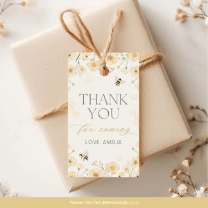 May include: A rectangular gift tag with the text "THANK YOU for coming LOVE, AMELIA". The tag features watercolor illustrations of yellow flowers and bees. The tag is tied to a wrapped gift with twine. The tag measures 5.08cm x 8.89cm.