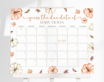 May include: A white easel displays a calendar-style sign with the text "guess the due date of BABY OLIVIA." The sign features watercolor pumpkins, leaves, and the calendar grid. The sign is decorated with orange and white pumpkins and fall foliage.