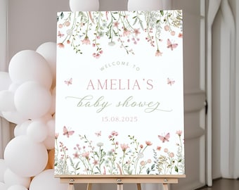 May include: Welcome to Amelia's baby shower sign with a floral design featuring pink and white flowers, butterflies, and green leaves. The text reads "Welcome to Amelia's baby shower 15.08.2025".