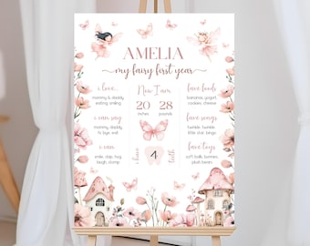 May include: A pink and white printable first birthday milestone chart with a fairy theme. The chart includes the child's name, Amelia, and details about their first year, including their height, weight, favourite foods, songs, and toys. The chart is decorated with butterflies, flowers, and a whimsical fairy house.