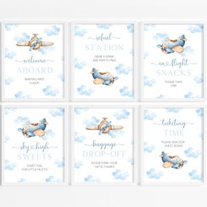 Op de afbeelding: Zes printbare borden voor een babyshower met een blauw en bruin vliegtuigthema. De borden zeggen "Welkom aan boord", "Tankstation", "Snacks tijdens de vlucht", "Hemelse snoepjes", "Bagage afgifte" en "Tickettijd".