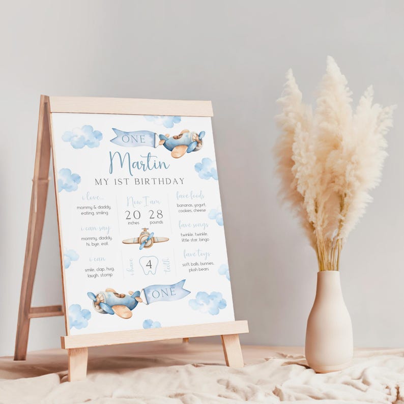 Puede incluir: Un cartel de primer cumplea&ntilde;os para un ni&ntilde;o de color azul y blanco con un tema de avi&oacute;n. El cartel incluye el nombre "Martin", la edad "Uno", y detalles sobre el primer a&ntilde;o del ni&ntilde;o, incluyendo su altura, peso, alimentos favoritos y actividades.