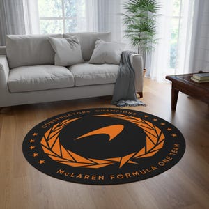 May include: A circular black rug with orange text reading "CONSTRUCTORS' CHAMPIONS" and "McLAREN FORMULA ONE TEAM". It has an orange laurel wreath design and a stylized orange logo.