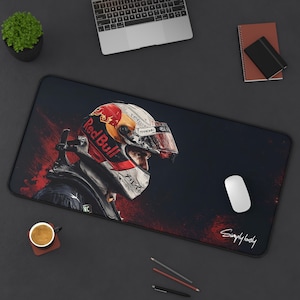 Może przedstawiać: Czarna prostokątna podkładka pod mysz z motywem kasku wyścigowego Red Bull. Kask jest biały, czerwony i żółty, z logo Red Bull. Biała mysz komputerowa leży na podkładce, z napisem "Simply lovely" w prawym dolnym rogu.