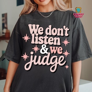 May include: A black t-shirt with the text "We don't listen & we judge" in pink with white stars around the text.