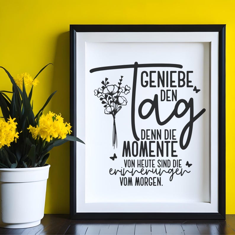 May include: A framed print with the German text "GENIE&szlig;E DEN Tag, DENN DIE MOMENTE VON HEUTE SIND DIE ERINNERUNGEN VOM MORGEN." The black and white design includes a floral bouquet and butterflies. A potted plant with yellow flowers sits to the left.