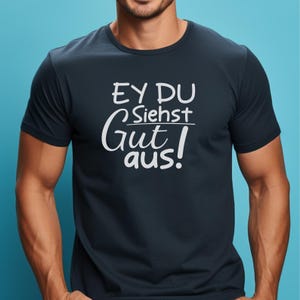 May include: Navy blue t-shirt with white text that reads "EY DU Siehst Gut aus!" in a casual font. The shirt has a crew neck and short sleeves. The text is centered on the chest.