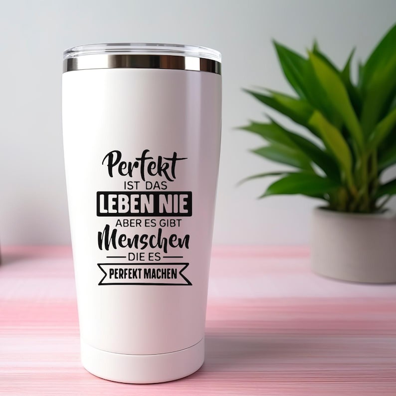 May include: A white stainless steel tumbler with a silver rim and lid. The tumbler features black text that reads "Perfekt ist das Leben nie, aber es gibt Menschen die es perfekt machen."