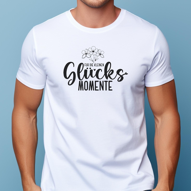 May include: White t-shirt with a black graphic design. The design includes the words "F&uuml;r die kleinen Gl&uuml;cks Momente" in a stylized font, along with a small floral illustration above the word "Gl&uuml;cks".