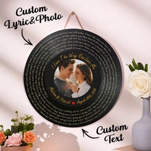 May include: A black circular photo plaque with a couple's photo in the center, surrounded by song lyrics. The plaque includes the text "I Love The Way You Love Me", "Madison & Patrick", and "August 25th, 2024". It is hanging by a brown string.