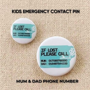 Könnte beinhalten: Zwei weiße, runde Anstecknadeln mit einer türkisfarbenen rechteckigen Grafik und dem schwarzen Text IF LOST PLEASE CALL, MUM: 017085766990 und DAD: 016487544339. Jede Nadel zeigt rechts neben dem Text eine kleine weiße Blumenillustration.