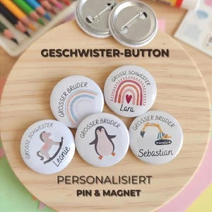 Op de afbeelding: Vijf ronde witte buttons met speldjes, voorzien van kleurrijke illustraties van een regenboog, een pinguïn, een hobbelpaard en een graafmachine. De tekst bevat namen zoals Lara, Leonie en Sebastian, samen met de Duitse termen Grosse Schwester en Grosser Bruder. Twee extra metalen achterkanten zijn bovenaan zichtbaar.