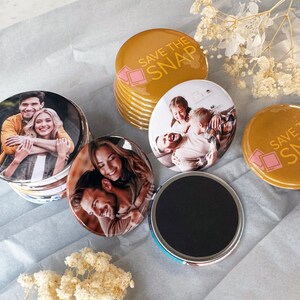 May include: A collection of round photo magnets featuring custom images of couples and families, alongside mustard yellow magnets printed with the text SAVE THE SNAP and a pink camera icon. Each magnet has a smooth, glossy finish and a black backing.