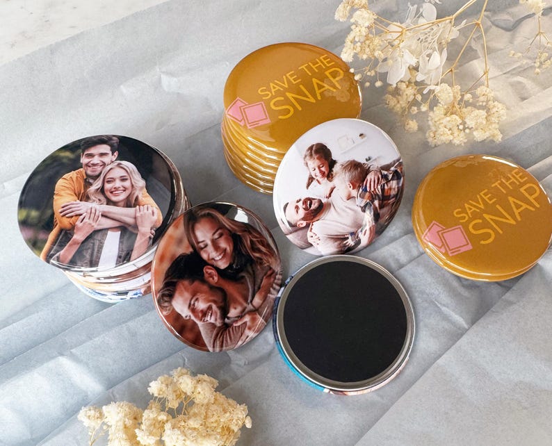 May include: A collection of round photo magnets featuring custom images of couples and families, alongside mustard yellow magnets printed with the text SAVE THE SNAP and a pink camera icon. Each magnet has a smooth, glossy finish and a black backing.