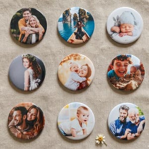 May include: A set of nine circular photo badges featuring various printed images, including couples, a person in a boat, a baby in a hat, a child with a flower crown, a parent and child, a child playing in sand, and two pairs of men.