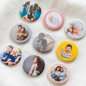 May include: A collection of eight circular pin-back badges featuring various personalised designs, including photographic portraits of individuals, couples, and children, alongside text elements such as names and dates printed on the badge edges.