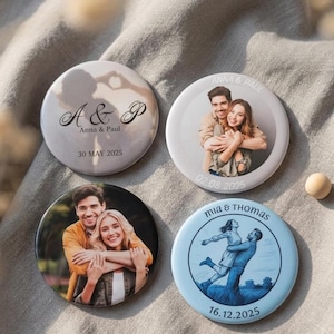 May include: Four circular custom pin-back buttons featuring personalised designs. Two buttons display photographic portraits of couples, one shows a silhouette with the text A & P Anna & Paul 30 MAY 2025, and one features a blue illustration of a couple.