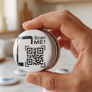 May include: A round white button featuring a black graphic of a smartphone outline and a QR code. The text "Scan ME!" is printed in black above the QR code. The button has a glossy finish and a metallic edge, presented as a circular pin-back badge.