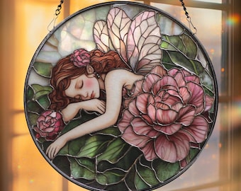 May include: Circular stained glass artwork depicting a sleeping fairy surrounded by pink roses and green foliage. The fairy has red hair and translucent wings. The piece is framed in black and suspended by a chain.