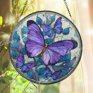 May include: A round stained glass window hanging featuring a design of purple butterflies and blue leaves. The butterflies have detailed wing patterns and are set against a light background. The window is framed with a black metal border and hangs from a chain.
