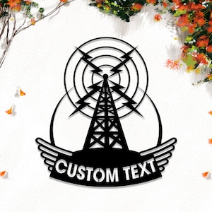 Könnte beinhalten: Ein schwarzes Wandkunstobjekt aus Metall, das die Silhouette eines zentralen Funkturms mit kreisförmigen Wellen und Blitzsymbolen zeigt. An der Basis befindet sich ein geschwungenes Banner mit dem weißen Text CUSTOM TEXT und Flügeln.