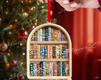 May include: A wooden bookshelf Christmas ornament with a red ribbon. The ornament features three shelves filled with colourful, floral-patterned books. The background includes a Christmas tree with red baubles.