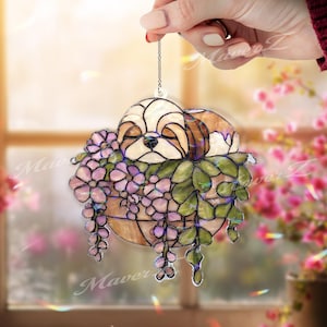 May include: A stained glass Shih Tzu dog in a hanging basket of purple flowers and green leaves. The dog has brown and white fur and is sleeping peacefully. The basket is a light brown colour and is suspended by a silver chain.