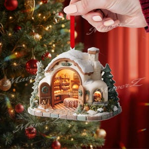 May include: A detailed Christmas ornament shaped like a bakery, featuring a snow-covered roof and a red ribbon for hanging. The interior is lit, showcasing shelves of bread and a small table. The ornament is surrounded by miniature trees and a stone path.