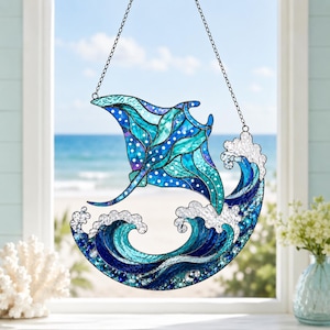 Puede incluir: Un atrapasoles de vidrieras que muestra una mantarraya nadando sobre olas oceánicas estilizadas. La pieza está hecha de varios tonos de vidrio azul, turquesa y blanco, suspendida por una fina cadena de metal, creando una escena acuática.