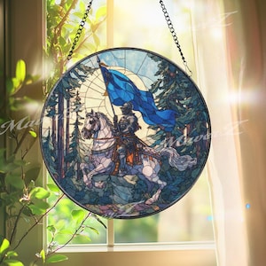 May include: Round stained glass window depicting a knight on horseback holding a blue flag. The knight is clad in armor, and the horse is white. The background features a forest scene with tall trees and a blue sky. The window is framed in black and hangs from a chain.