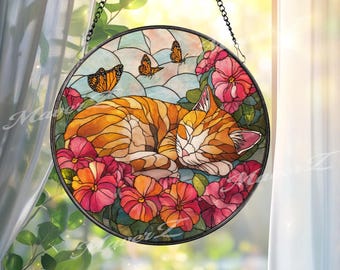 Puede incluir: Vidriera redonda que representa un gato atigrado naranja durmiendo rodeado de flores rosas y naranjas. Tres mariposas naranjas están en el fondo. La ventana está enmarcada en negro y cuelga de una cadena.