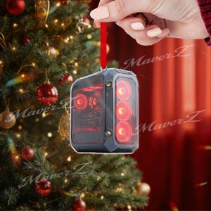 May include: A computer case ornament with red LED lights and a clear side panel, hanging from a red ribbon. The ornament is held by a hand in front of a Christmas tree.
