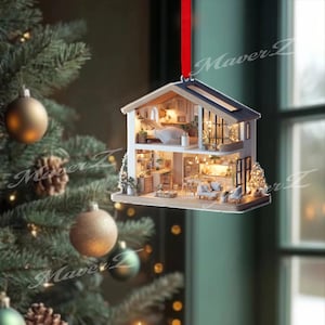 May include: A two-story house-shaped Christmas ornament featuring an open-concept interior with miniature furniture, warm interior lighting, and a red ribbon hanger. The structure displays a bedroom on the top floor and a living area below.