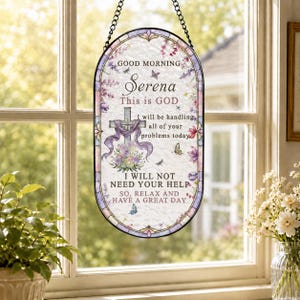 Könnte beinhalten: Ein ovales Hängeschild aus Buntglas mit einer schwarzen Kette. Das Design zeigt ein Kreuz, florale Akzente und Schmetterlinge. Der Text lautet: GOOD MORNING Serena This is GOD I will be handling all of your problems today I WILL NOT NEED YOUR HELP.
