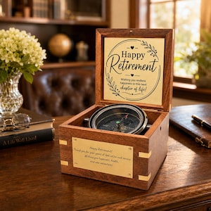 May include: A dark wood box with a hinged lid containing a metal compass. The inside lid features text reading Happy Retirement Wishing you endless happiness in this next chapter of life. A brass plate on the front reads Happy Retirement Thank you for your years of dedication and service. Wishing you happiness, health, and new adventures.