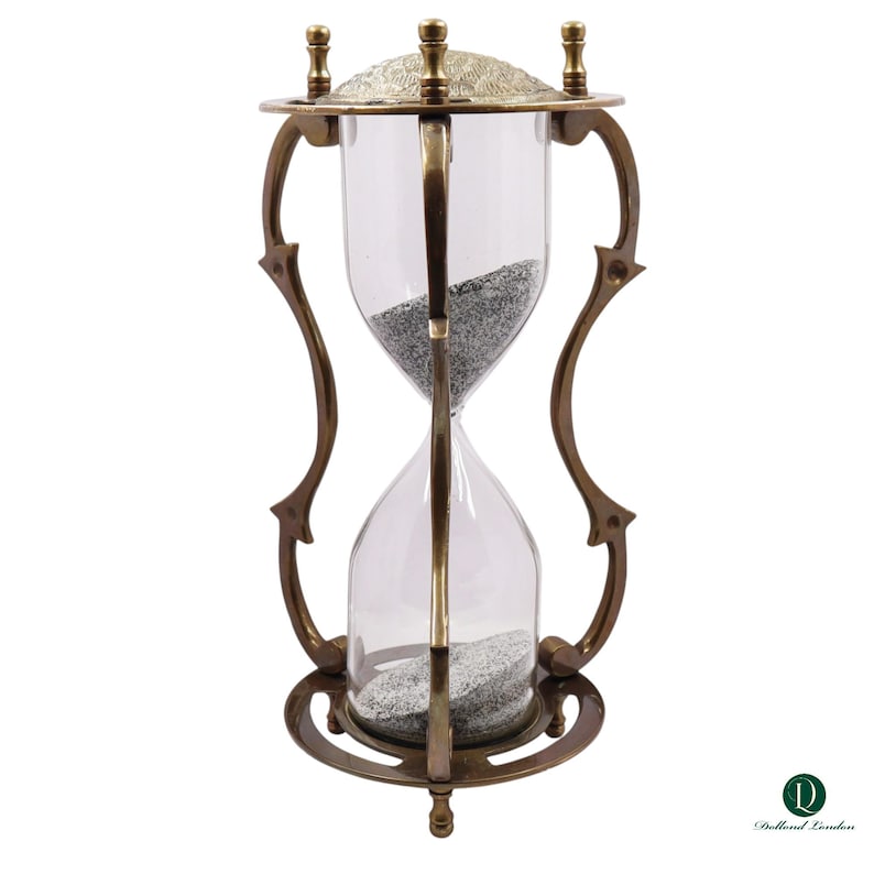 Puede incluir: Un reloj de arena con marco de lat&oacute;n, soportes curvos y una placa superior texturizada. Los bulbos de vidrio transparente contienen arena gris. La base y la parte superior son circulares, y la estructura se mantiene mediante varillas de lat&oacute;n. El logotipo Dollond London es visible en la esquina inferior derecha.