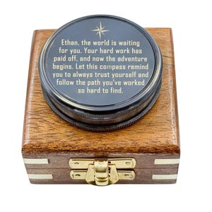 May include: A round, dark-toned compass with a gold star icon and engraved text that reads: Ethan, the world is waiting for you. Your hard work has paid off, and now the adventure begins. Let this compass remind you to always trust yourself.