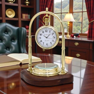 May include: A brass desk clock with a white clock face and black numerals. The clock is suspended within a brass arch and sits on a dark wood base. A magnifying glass is at the base. The clock reads "London".