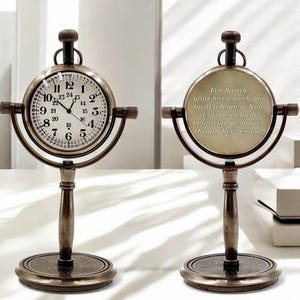 Peut inclure: Une horloge de bureau de style vintage avec un cadran rond et des chiffres romains. L'horloge a une finition bronze et une base décorative. Le cadran affiche l'heure. Le texte au dos dit: "Pour Sarah, votre dur labeur a construit un héritage. Il est maintenant temps de construire de beaux souvenirs. Joyeuse retraite!"