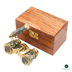 May include: A pair of antique brass opera glasses with iridescent mother-of-pearl accents, next to a wooden box with a brass clasp. The opera glasses have a gold finish and are designed for viewing performances. The wooden box is a rich brown color.